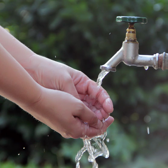 Washing hands under open spigot outside in springtime